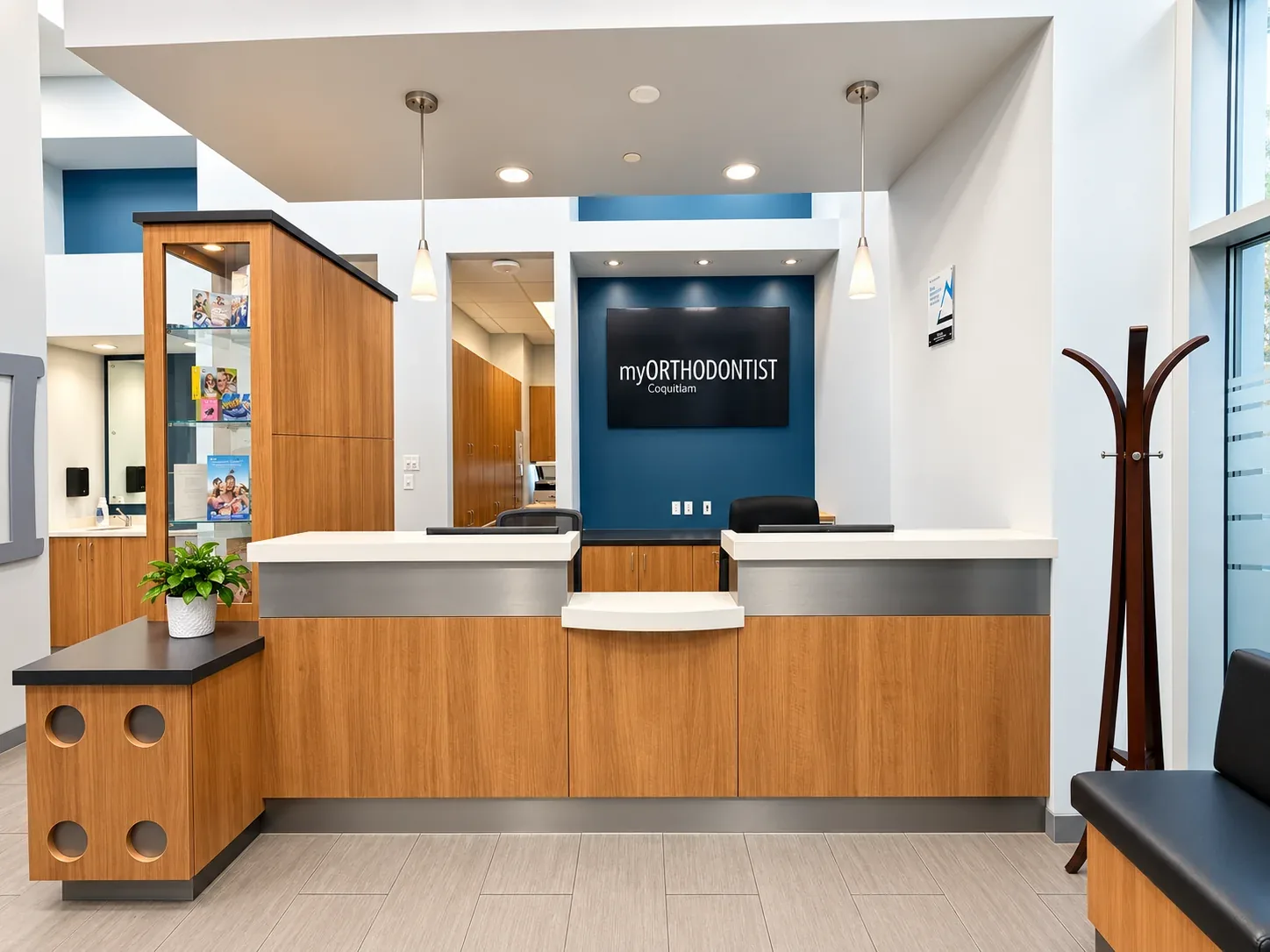 Reception interior at myORTHODONTIST Coquitlam with wood cabinetry, blue accent wall, pendant lighting, and clinic signage